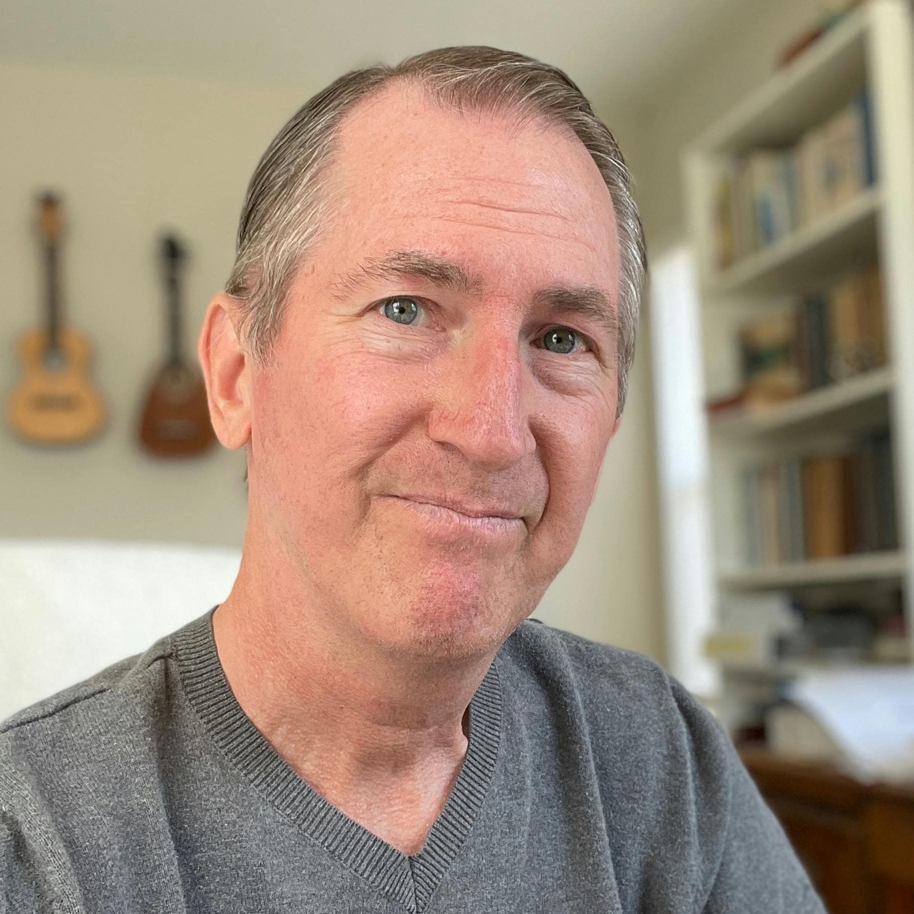Kevin bergen therapist, with gray shirt, and string instruments on wall and bookshelf behind him