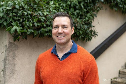 author of the article jonathan newsum. in orange shirt sweater and blue under shirt with green in background